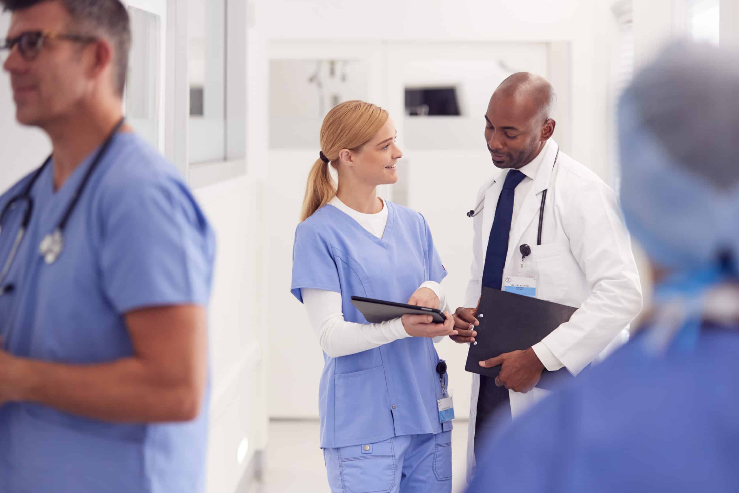 doctor in white coat and nurse in scrubs looking at digital tablet in hospital corridor